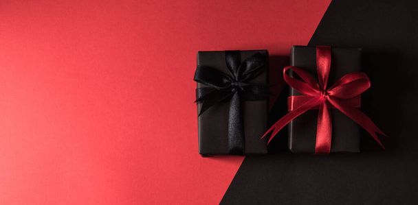 Black Friday sale shopping concept, Top view of gift box wrapped in black paper and black bow ribbon, studio shot isolated on red and dark background - Valokuva, kuva