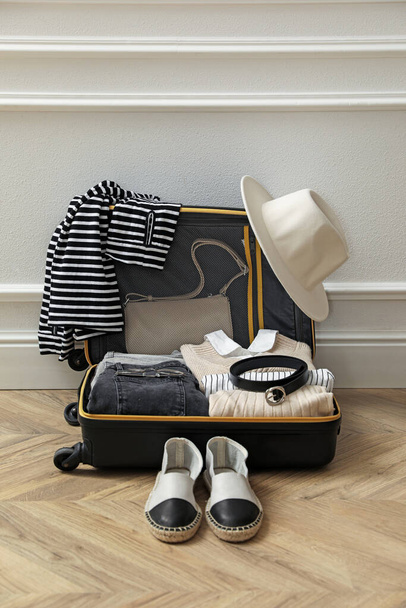 Open suitcase with folded clothes, accessories and shoes near white wall indoors - Zdjęcie, obraz
