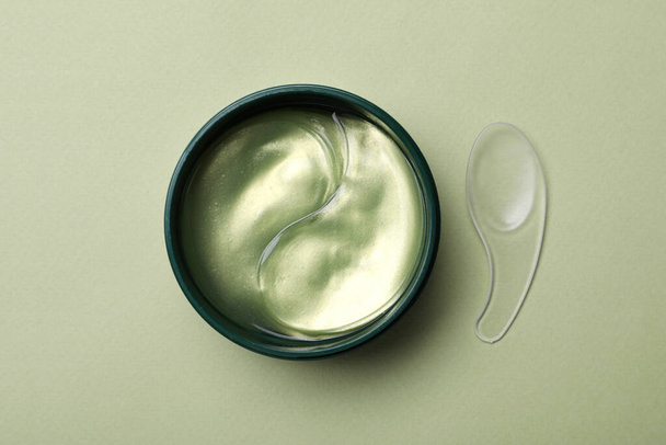 Under eye patches in jar and spatula on olive background, flat lay. Cosmetic product - Fotografie, Obrázek