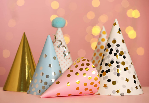 Beautiful party hats on pink table against blurred festive lights - Photo, Image