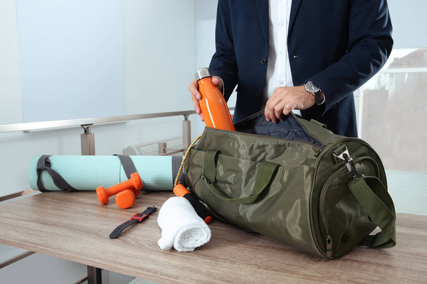 Businessman packing sports stuff for training into bag in office, closeup - 写真・画像