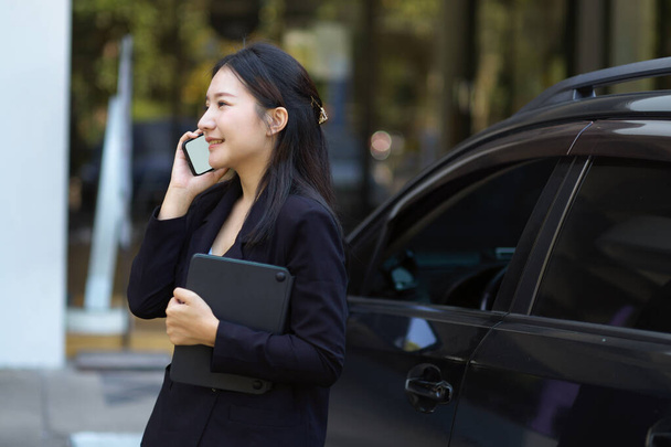 Una empresaria segura y exitosa hablando por teléfono, parada cerca de su coche. Vida urbana y concepto de empresarios. - Foto, imagen
