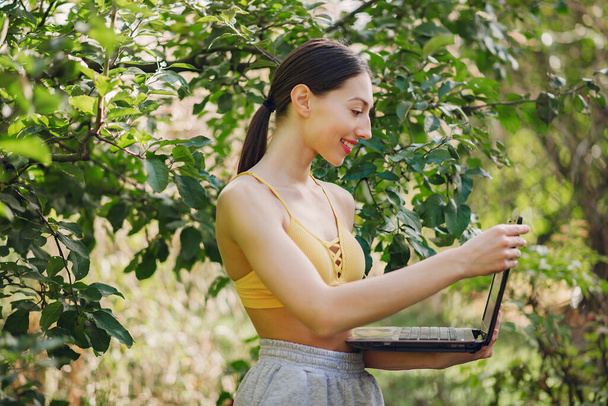 Girl standing in a summer park and holding a laptop in her hands - Foto, immagini