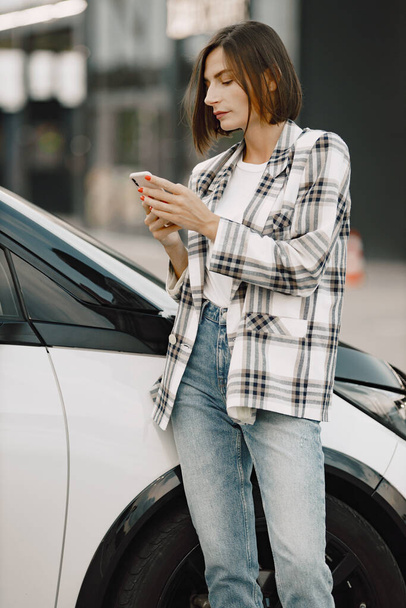Προσωπογραφία νεαρής μελαχρινής γυναίκας που χρησιμοποιεί κινητό κοντά στο αυτοκίνητό της - Φωτογραφία, εικόνα