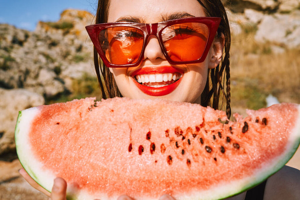 cheerful woman in sunglasses and watermelon nature rocks - Foto, afbeelding