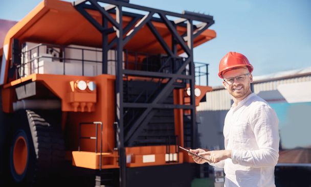 Giovane ingegnere in casco con tablet computer in mano sullo sfondo di camion per minerale di estrazione del carbone - Foto, immagini