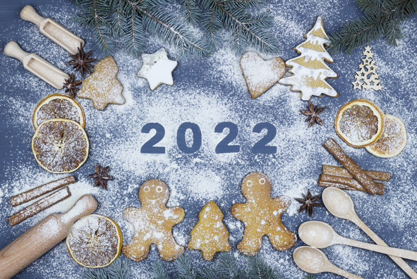 ハッピーニューイヤー2022小麦粉で書かれています。調理のための成分とクリスマスベーカリーの背景。彼らは小枝、ジンジャーブレッド、小さな男を食べた。小麦粉、スパイス、おもちゃのトップビュー. - 写真・画像