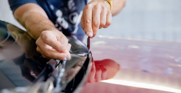 Konzept Transparenter Schutz für Farbe. Prozess der Verklebung der Motorhaube eines roten Autos mit einer schützenden Vinylfolie vor Kiesabsplittern und Kratzern - Foto, Bild