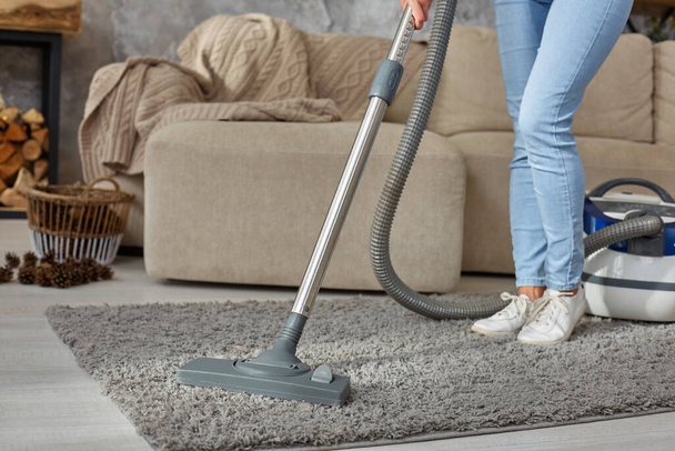 Cropped image of beautiful young woman using a vacuum cleaner while cleaning carpet in the house - Photo, image