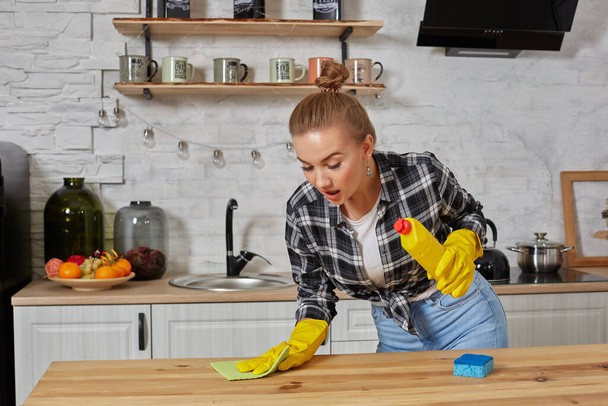 Lastik eldivenli genç kadın ya da ev hanımı mutfak mutfağında mikrofiber bezle masayı siliyor.. - Fotoğraf, Görsel