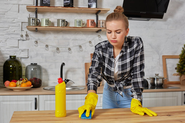 Mladá žena v ochranných rukavicích utírá stůl v kuchyni hadrem - Fotografie, Obrázek