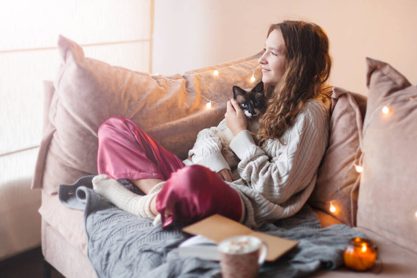 Morning, leisure, Christmas, winter and people concepts - happy young woman with cat and cup of coffee or tea in a cozy living room. Female at home - Фото, зображення