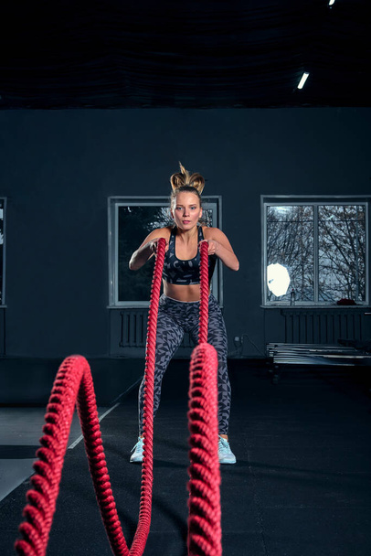Vertical full length shot of an athletic fitness woman doing functional training exercise with battle ropes at the gym Cross Fit cross training strength endurance energy power concept - Foto, Bild