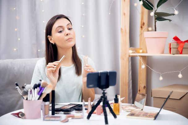 Mutlu kadın vlogger telefonda video kaydı yaparken kozmetik ürünleri gösteriyor. Influencer blog yazarı güzellik günlüğünü kavra - Fotoğraf, Görsel