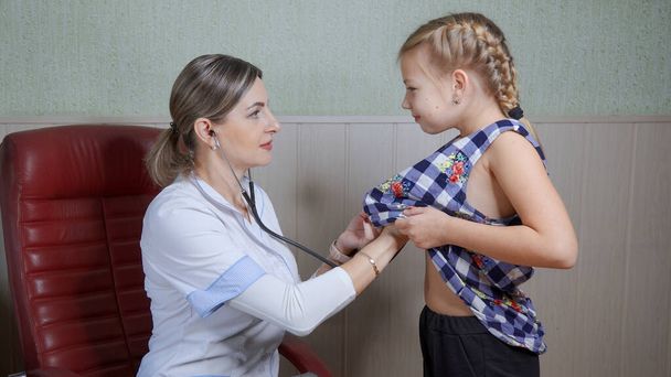Positive female pediatrician listening to the lungs of a young girl with a stethoscope. Child health care concept. - Photo, Image
