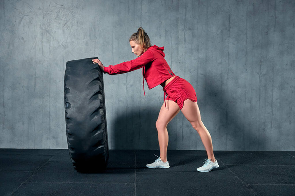Подходящая спортсменка, тренирующаяся с огромной шиной. Вид сбоку. Женщина занимается силовыми упражнениями. - Фото, изображение