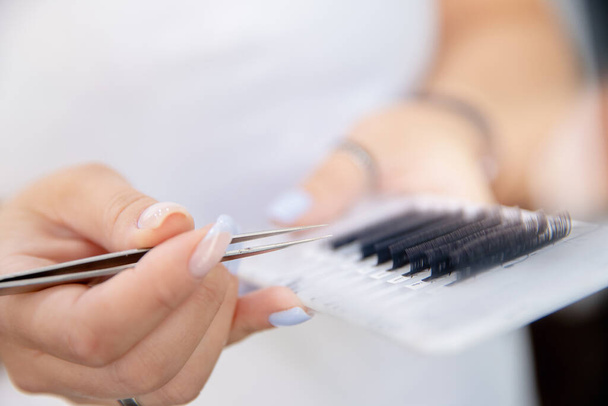 Eyelash extension master holds tweezers and palette of materials in his hands - Photo, Image