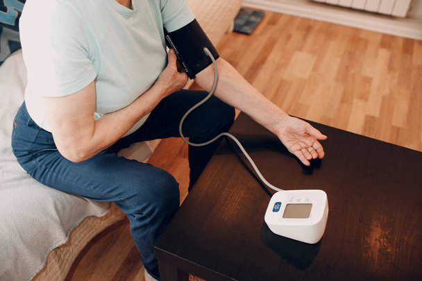 Mujer mayor tomando medidas de presión arterial en casa. Autocuidado de la salud de los ancianos - Foto, imagen