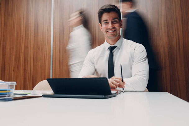 ラップトップを使用しているビジネスマンは、オフィスミーティングの背景にあるテーブルに座って、動きのある人を歩きます。ビジネスマンと女性グループの会議の議論 - 写真・画像