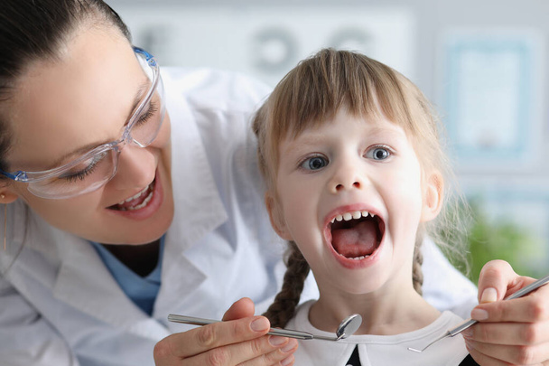 Aranyos gyerek látogató család orvos és nyitott szájú gyermekorvos szerszám ellenőrzés fáj a torkát - Fotó, kép