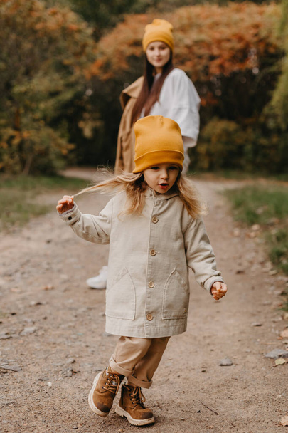 Young happy and smiling mom with her little daughter in arms hugging and kissing spending a weekend on a walk in autumn park. selective focus, noise effect, Autumnal mood - Foto, Imagen