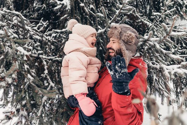 Happy loving family! Father and his baby are playing and hugging outdoors. Little child and daddy on a snowy winter walk in nature. Concept of the first long-awaited winter snowfall. copy space - 写真・画像
