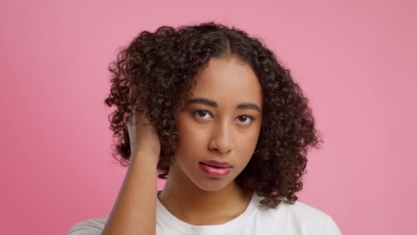 Afroamerykanka dotyka kręcone włosy figlarnie na różowym tle - Materiał filmowy, wideo