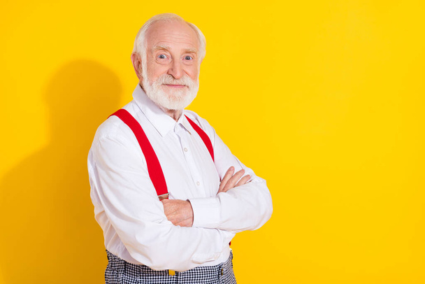 Photo of funny aged grey hair man crossed hands wear white shirt suspenders isolated on yellow color background - Foto, Imagem