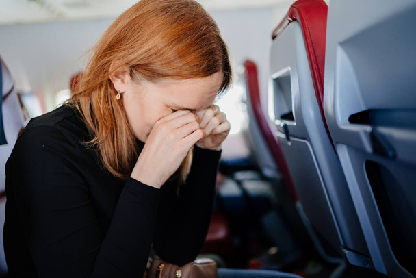 a sleepy woman rubs eyes with hands in an airplane seat. long flights. - Фото, изображение