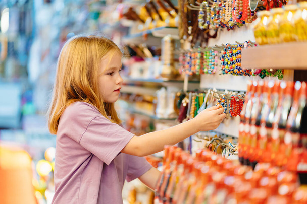 a funny little girl looks with interest at jewelry and souvenirs in the store.  - Zdjęcie, obraz
