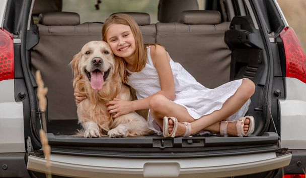 Preteen girl with golden retriever dog in car trunk - Valokuva, kuva