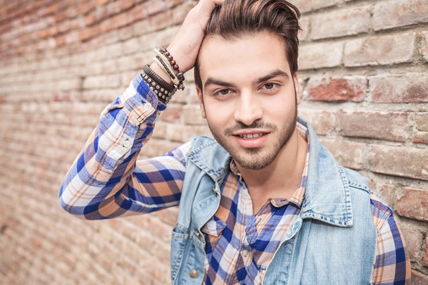 young man fixing his hair, leaning on a brick wall - Photo, image