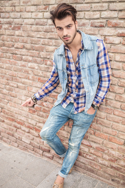 Homem de jeans apoiado numa parede de tijolos
 - Foto, Imagem