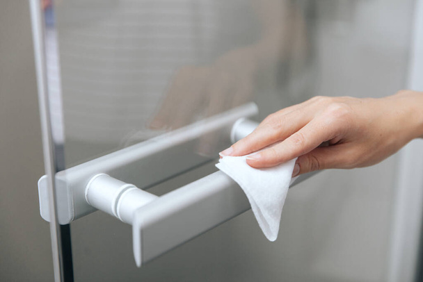 Cleaning glass door handles with an antiseptic wet wipe. Sanitize surfaces prevention in hospital and public spaces against corona virus. Woman hand using towel for cleaning home room door link - Valokuva, kuva