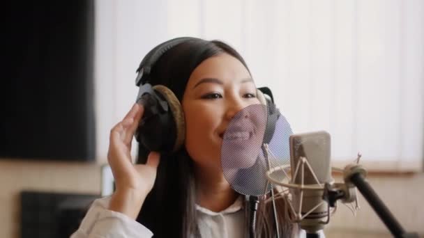 Asian Female Musician Wearing Headphones Singing Song To Microphone In Music Studio - Felvétel, videó