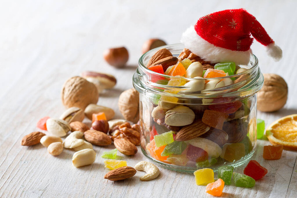 Christmas mix of nuts and candied fruits in glass jar on white wooden background - Photo, Image