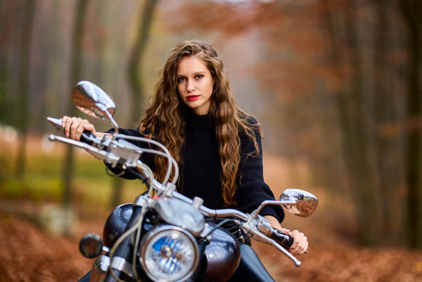 Красива жінка з довгим волоссям на подрібненому мотоциклі в осінньому пейзажі
. - Фото, зображення