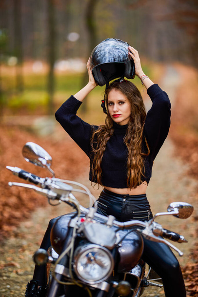 A beautiful woman with long hair on a chopper motorcycle in autumn landscape. - Fotó, kép