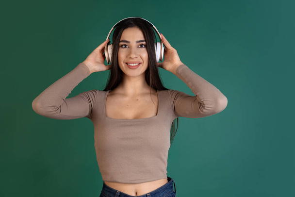 Cropped portrait of happy and delightful young woman listening to music in headphones isolated over green background - Photo, image