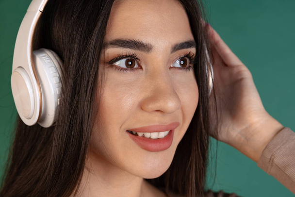 Close-up portrait of beautiful young woman, girl in white headphones isolated over green background - Valokuva, kuva