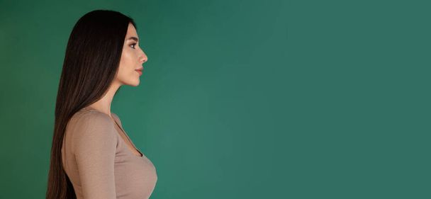 C ropped vista lateral retrato de menina atraente jovem olhando em linha reta, posando isolado sobre fundo verde. Folheto - Foto, Imagem