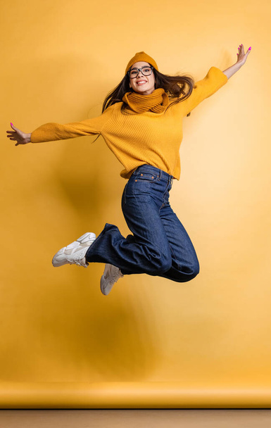 Ganztägiges Porträt eines glücklichen und aufgeregten jungen Mädchens in buntem Tuch, das isoliert über gelben Hintergrund springt - Foto, Bild