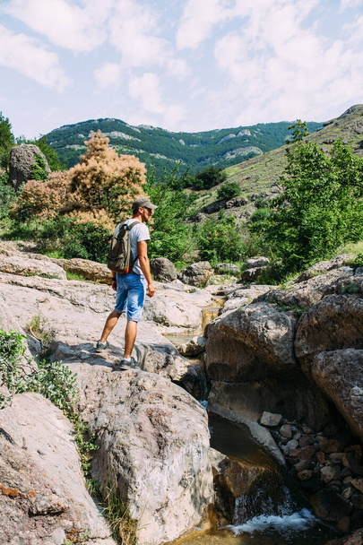 Fiatalember utazó sétál egyedül a hegyi folyó sziklás nyári táj - Fotó, kép