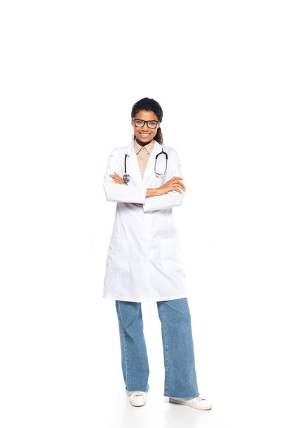 Tam boy gülümseyen Afro-Amerikan göz doktoru beyaz arka planda kollarını kavuşturuyor. - Fotoğraf, Görsel
