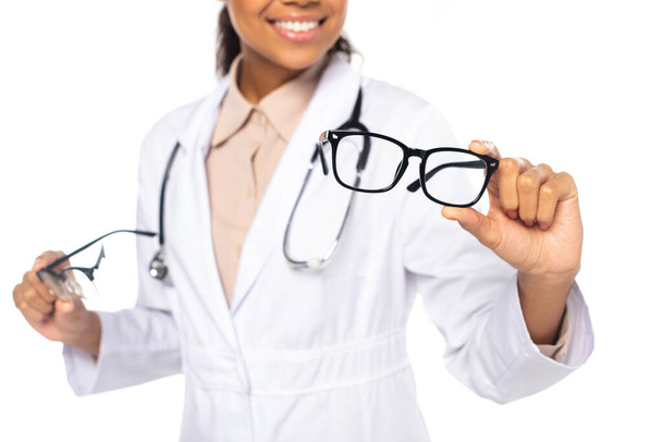 Cropped view of blurred african american doctor holding eyeglasses isolated on white  - Фото, зображення