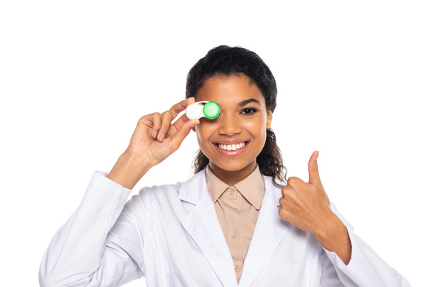 Lächelnder afrikanisch-amerikanischer Augenarzt zeigt wie und hält Behälter mit Kontaktlinsen isoliert auf weiß  - Foto, Bild