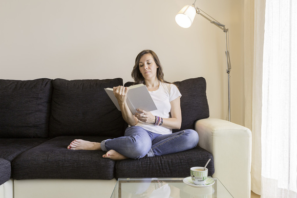 jovem mulher lendo um livro em um sofá - Foto, Imagem