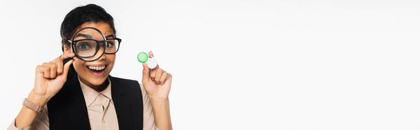 Веселая африканская американская бизнесвумен держит увеличительное стекло и контактные линзы изолированы на белом, баннер  - Фото, изображение