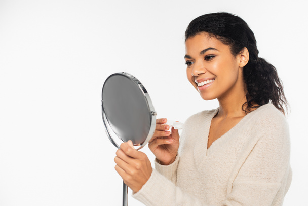 Smiling african american woman holding mirror and contact lenses isolated on white - 写真・画像