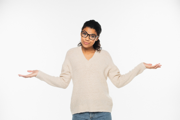 Confused african american woman in sweater and eyeglasses doing shrug gesture isolated on white - Foto, afbeelding